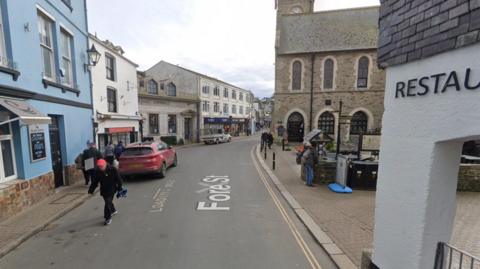 A narrow Cornish street with a blue pub on the left and a granite church on the right.