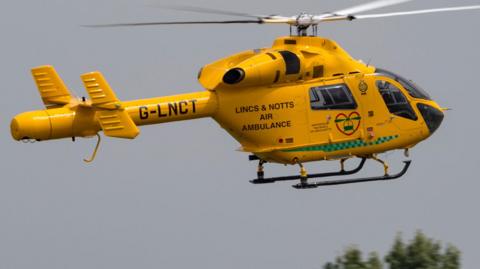 A yellow helicopter in mid flight. The sky is grey