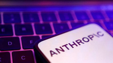 A smartphone display showing the Anthropic logo in black letters on an all-white background, laid on a laptop keyboard lit in pink and purple