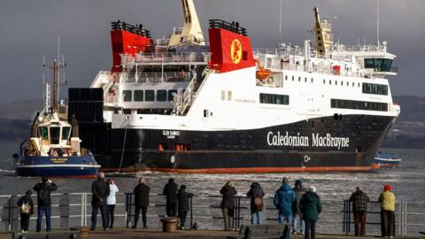 people on the harbourside look at a calmac ferry