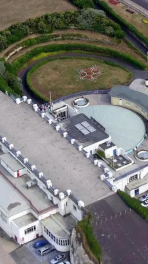 Aerial shot of large grey building on cliff edge