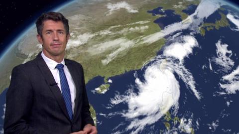 Chris Fawkes in front of a satellite image of Typhoon Krathon