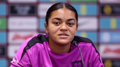 Jess Carter has swept back hair and a bright pink England shift with black stripes along the shoulder and sleeves