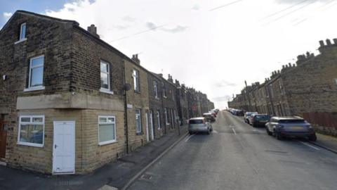 A street with a row of terraced houses on both sides with cars parked on the roadside.