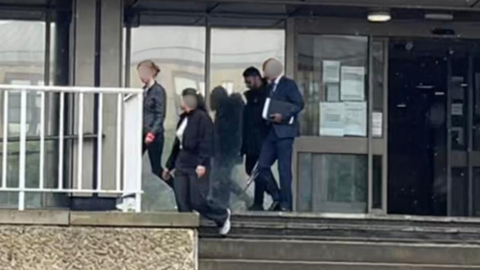 Four people walking from a court building. Three of their faces are blurred.