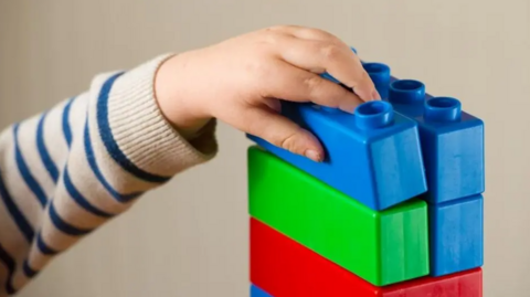 Hand of child building a tower of colourful Duplo blocks 