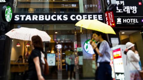 The shopfront of a Starbucks branch in Seoul with people walking in front of it 