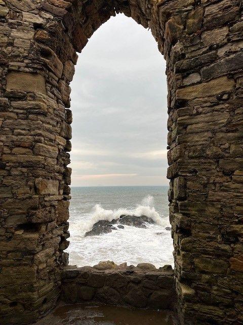 waves crashing against a rock visible through a gap in a stone wall