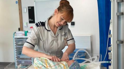 A woman wraps a baby in a blanekt in a mock maternity ward.