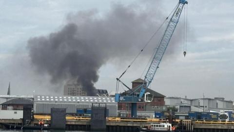 Smoke pouring over the top of some warehouse buildings