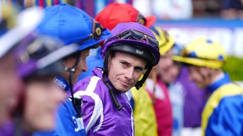Ryan Moore in racing colours - looking at the camera wearing a purple top and a helmet