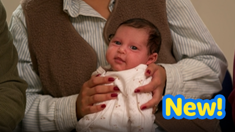 Baby being held on a caregiver's knee smiles towards the camera