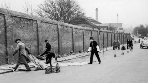 A black-and-white image of police moving items on a street.