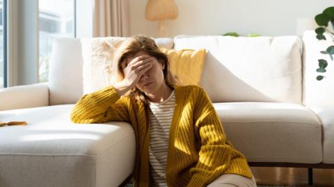 Woman having headache and holding her head while sitting on the floor at home