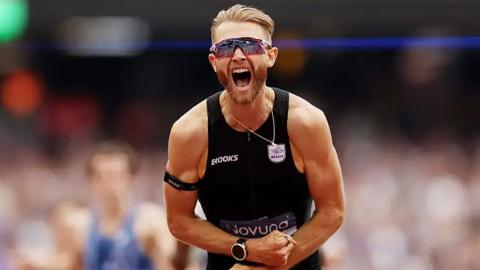 Josh Kerr wearing an athletics jersey yelling in a crowded sports stadium