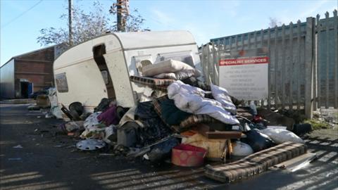Fly-tipping rubbish, including mattresses and bedding, piled up against an old white caravan