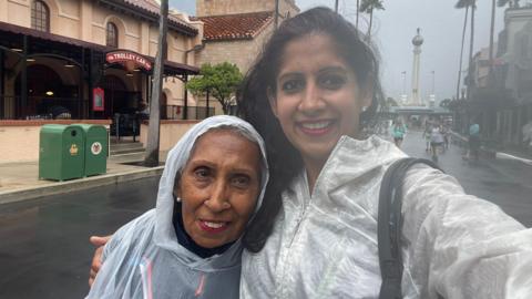 Minreet and her mum Pritpal smile at camera in the rain whilst wearing ponchos 