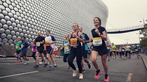 Male and female runners running past Selfridges building in Birmingham city centre. 