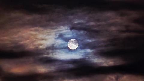 Atmospheric image of full Moon photographed in night sky between parting of clouds