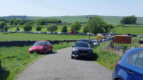 Cars parked on a road with green fields either side