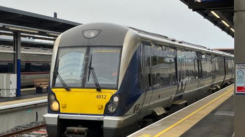 A translink train, painted yellow, blue and grey, stationary on the rail lines at Belfast's Grand Central Station