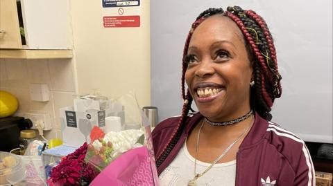 Jessica Bonner smiling and posing for the camera. She is wearing a red adidas jacket and holding a bouquet of flowers. 