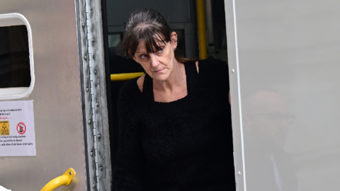 A woman with dark hair walking out of a police van. She had a black jumper dress on