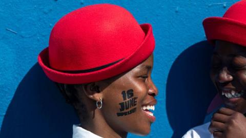 Dancers wearing red hats wait to perform on the anniversary of the Soweto Uprising.