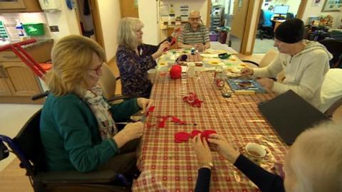 Residents at a hospice are sitting round a table cutting felt together as part of a group activity.