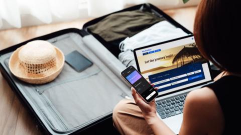 A young woman booking flight and hotel online with laptop and smartphone.