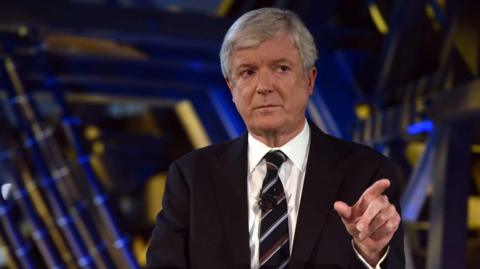 Lord Tony Hall looks stern and points off camera during a BBC event.