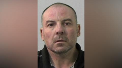 Mugshot of William Gardner. He has a shaved head and very short stubbly beard.