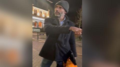 Photo of man in black jacket and grey hat with orange carrier bag