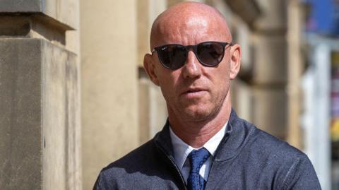 Nicky Butt, wearing sunglasses, a blue cardigan and a blue shirt and tie, outside Blackburn Magistrates Court