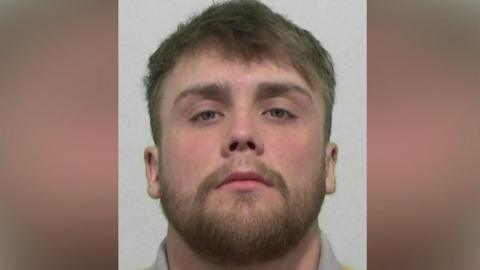 Mugshot of Kennedy. He has a short thick fair beard and short thick fair hair