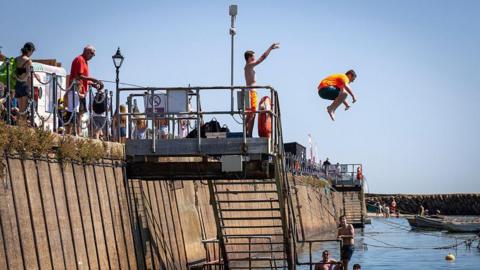 Teenage boys jumping from the harbour wall into the water during the ongoing Summer heatwave.