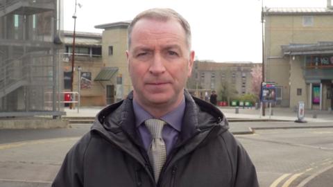 A man wearing a purple shirt and a silver tie looking towards the camera