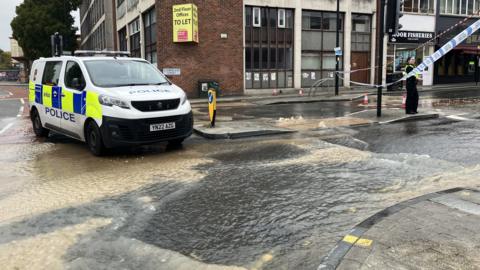 A police van is parked at the corner of a flooded road. A police officer can be seen standing to the right of the picture