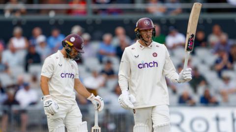 George Bartlett holds his bat aloft after reaching a half century
