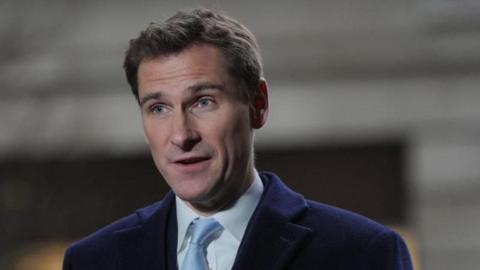 A man with short hair wearing a blue jacket, white shirt and light blue tie