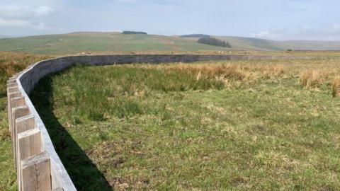 A timber fence built in a field. The fence begins to the left of the image and as it advances into the distance it curves to the right.