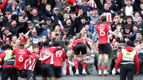 Lincoln City players, wearing their red and white home shirt, celebrate the winning goal over Wimbledon with their jubilant fans