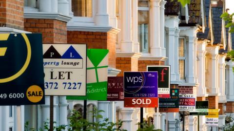 Lots of for sale and lettings signs on a street of terraced houses.