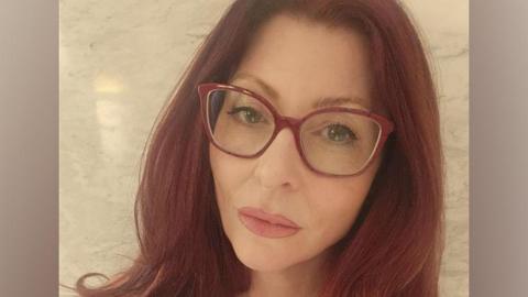 Teana Lynne has long red hair and red-framed glasses in this selfie.