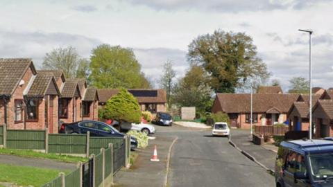 A small cul-de-sac with bungalows on both sides and a number of cars parked outside