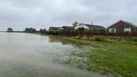 A badly flooded field in Fiskerton, with homes in the background. The water has almost reached the garden fences.