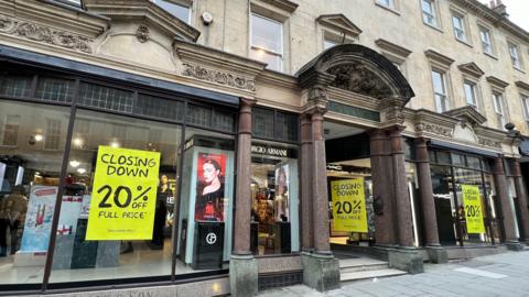 A shop front of a department store with yellow 'Closing Down' posters in the window.