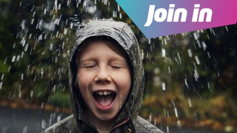 A child smiling in waterproofs as it rains on them