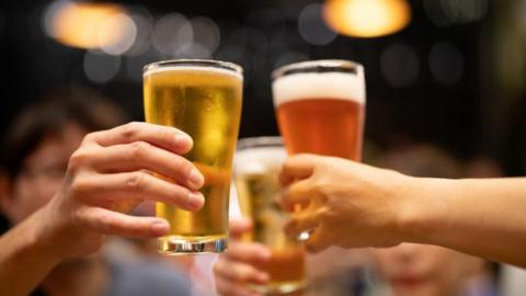 Three friends hold their beer glasses together in a toast