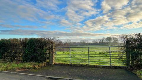 Blue skies and sunny spells with patchy cloud. A green field lies behind a farm gate.